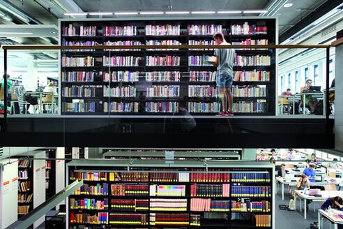 Innenansicht der Universitätsbibliothek mit Tischen und vollen Bücherregalen