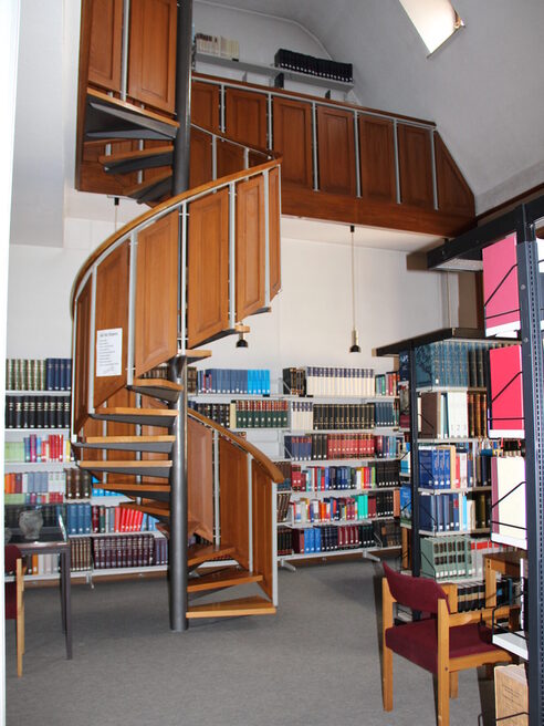 Innenansicht der Bibliothek mit Wendeltreppe und vollen Bücherregalen