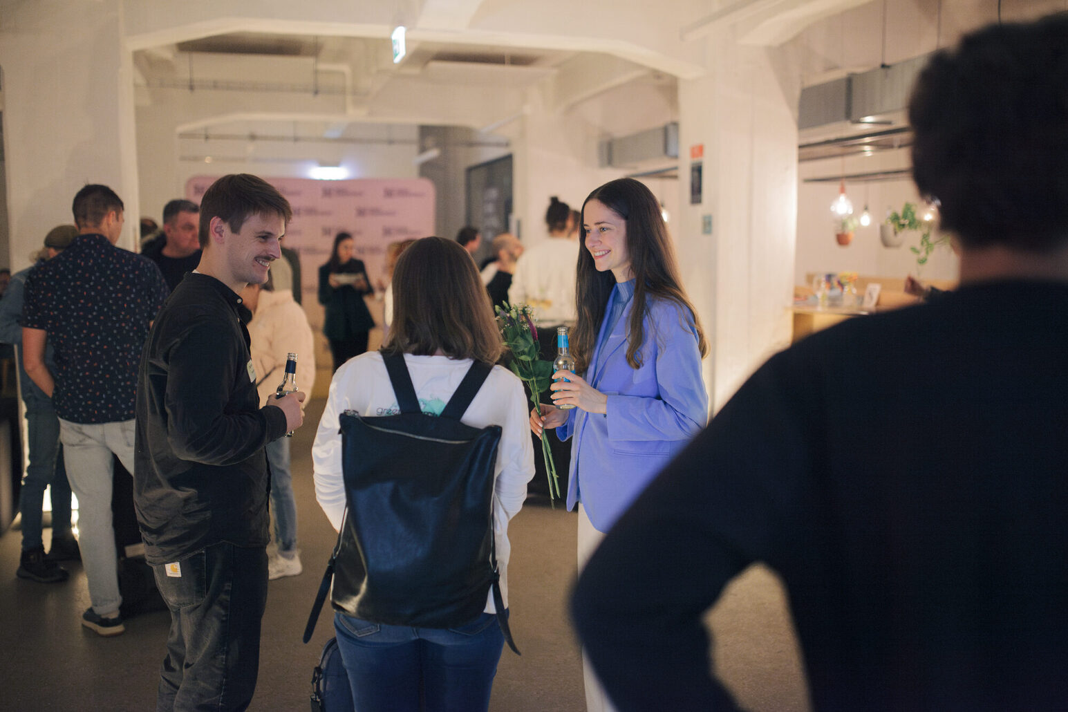 Un grupo de personas conversa animadamente. Un hombre permanece en primer plano de espaldas al espectador.