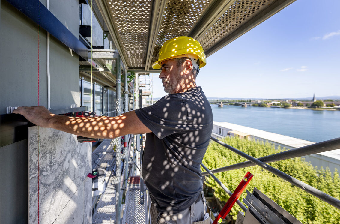 Bir inşaat işçisi belediye binasının dış cephesinde iskele üzerinde çalışıyor