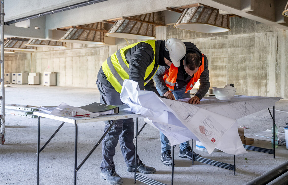 İki inşaat işçisi bina planını inceliyor.