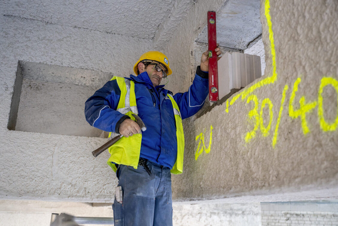 Elinde su terazisiyle içeride bir inşaat işçisi.