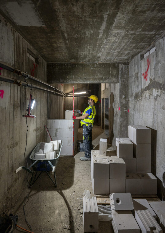 Beton elemanlarla çevrili dar bir koridorda inşaat işçileri.