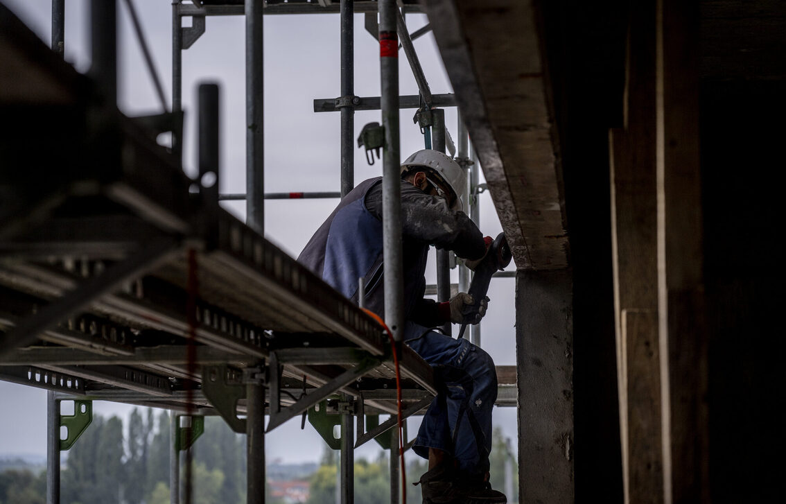 İnşaat işçisi iskele üzerinde oturuyor ve dış cephede çalışıyor.