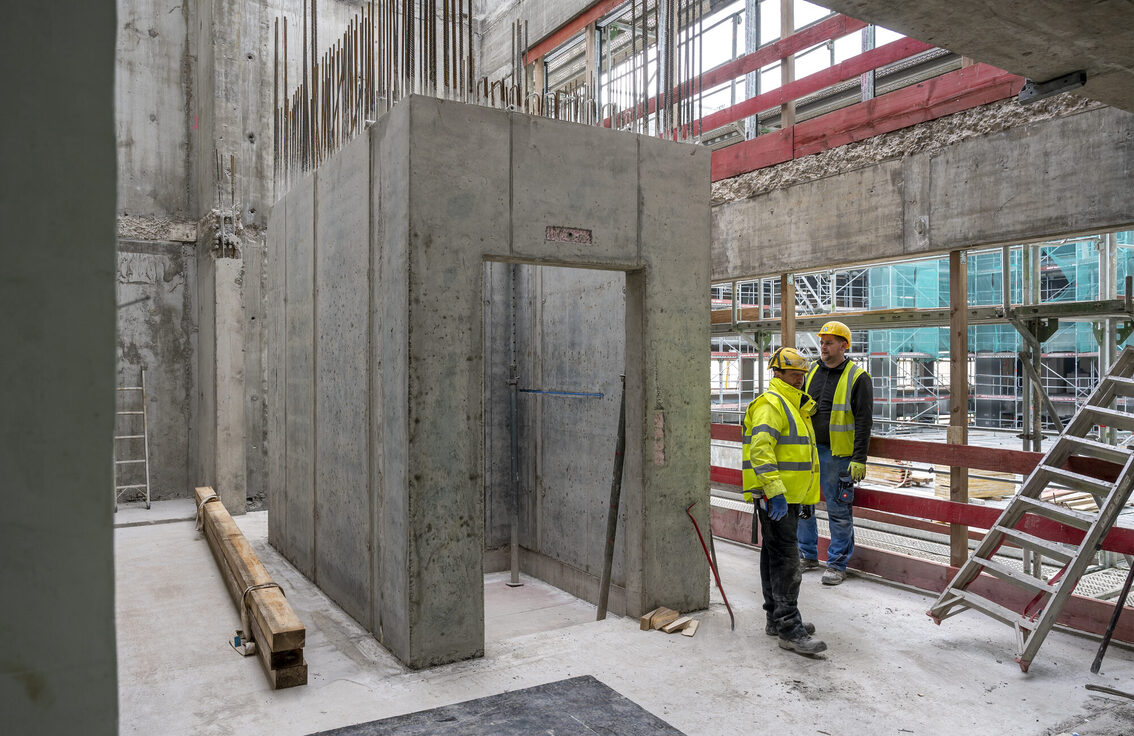 İki inşaat işçisi belediye binası şantiyesinde duruyor.