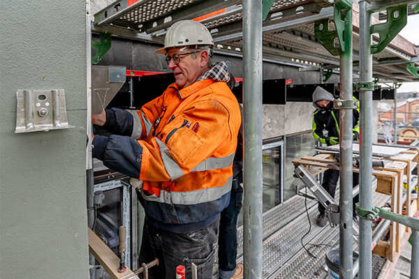 İki inşaat işçisi iskele üzerinde duruyor ve belediye binasının dış cephesinde çalışıyor