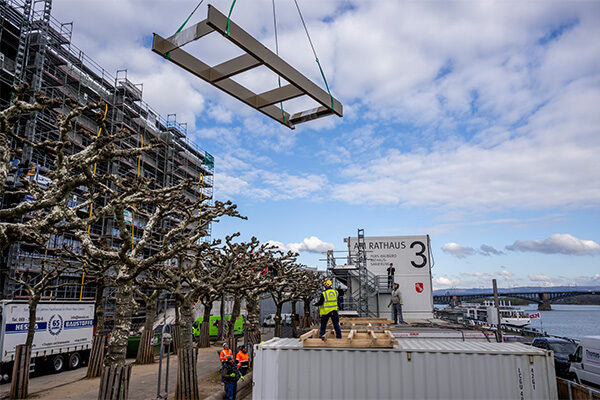 Sağda Ren Nehri, ortada konteynerler, solda belediye binası şantiyesi ve yukarıda ipte asılı bir güneşlik.