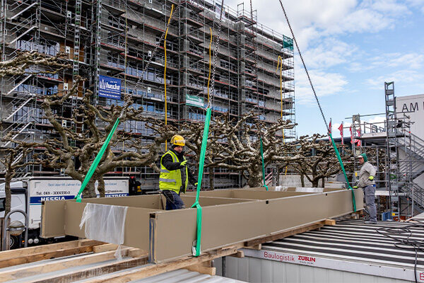 İki inşaat işçisi vinçten bir güneş koruma ızgarası indiriyor.