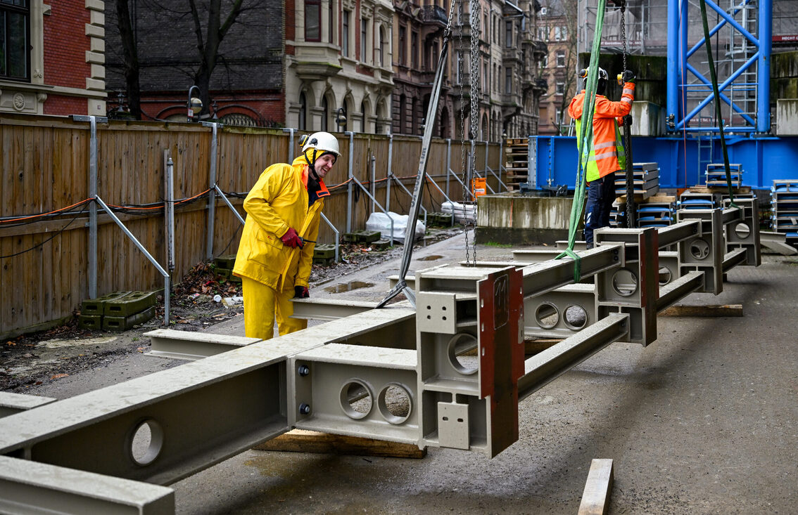 İki inşaat işçisi büyük bir çelik parçayı halatlara bağlıyor