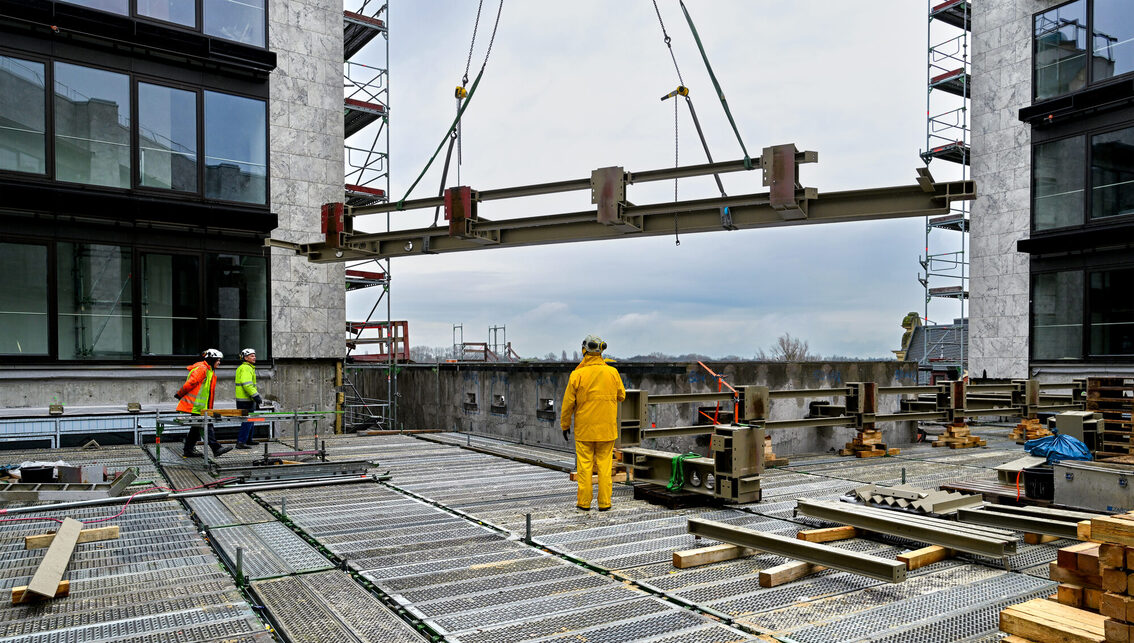 Belediye binasının şantiyesinde çalışan üç inşaat işçisi bir çelik parçasını teslim alıyor.