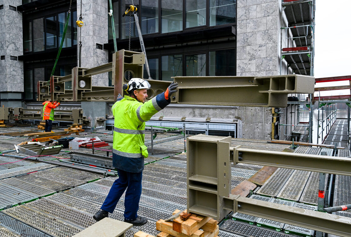 İnşaat işçileri belediye binası şantiyesinde çelik bir parçayı teslim alıyor