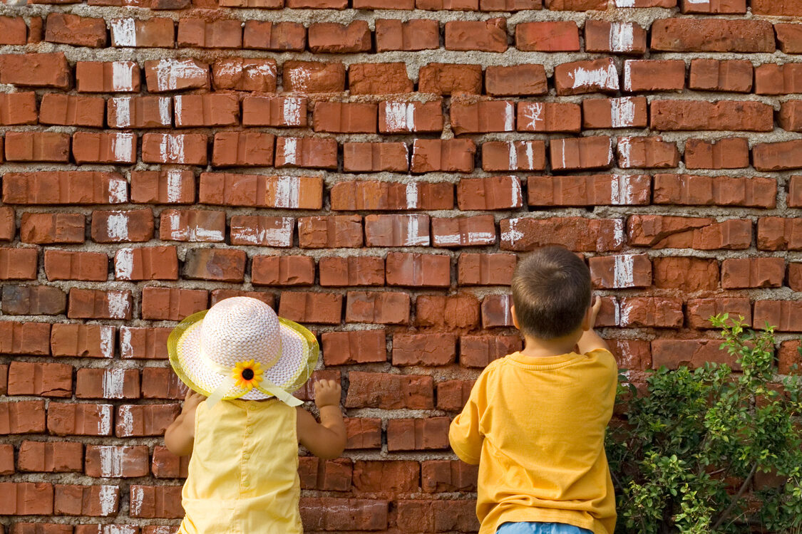 Deux enfants dessinent une maison à la craie sur un mur