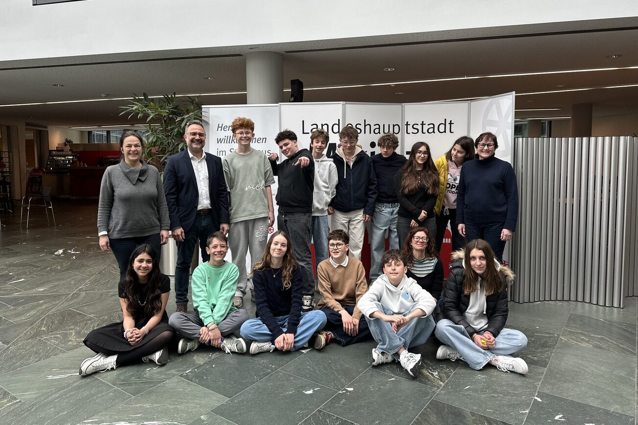 Gruppo di persone nell'atrio del Municipio di Magonza: un insegnante a sinistra, uno a destra. La seconda persona da sinistra: il direttore del dipartimento scolastico Delbasteh. In mezzo 14 studenti di scambio