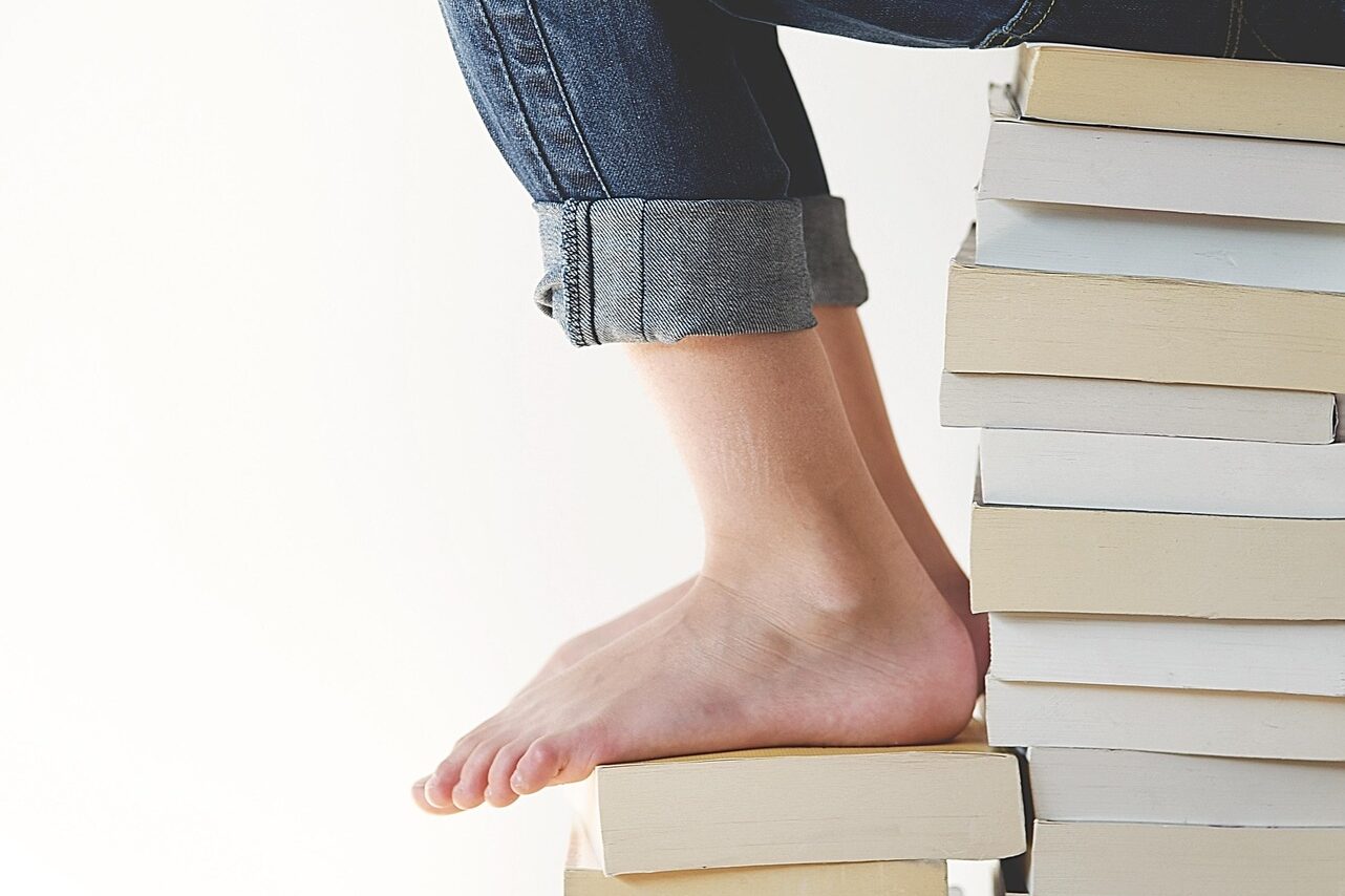 Two tall stacks of books can be seen. A person is sitting on one of them and reading.