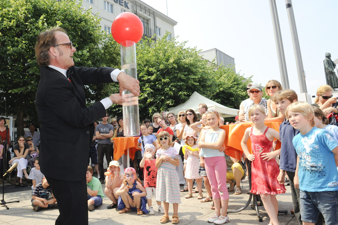 Науковий ярмарок 2011 року з чоловіком на передньому плані, який проводить експеримент з прозорою трубкою, діти дивляться на нього.