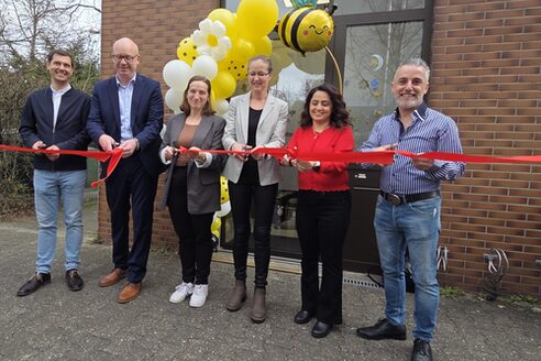 Sei persone si trovano davanti al centro diurno e tagliano un nastro rosso per celebrare l'apertura.