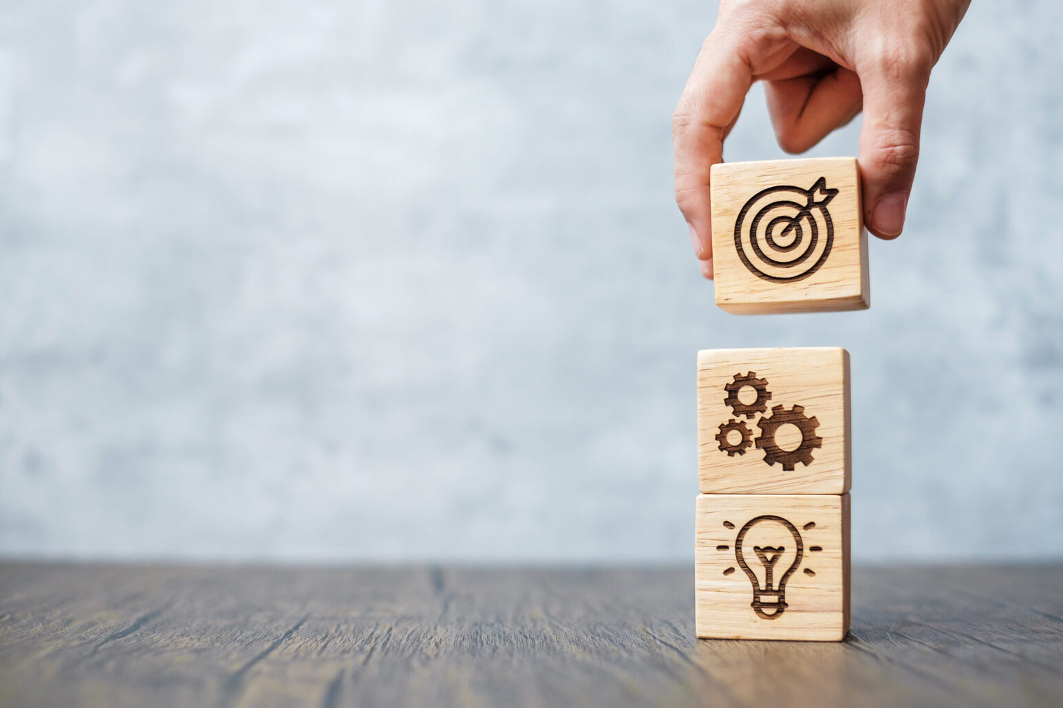 Une main empile des cubes en bois sur lesquels sont gravés des ampoules, des bords de dents et un jeu de fléchettes.