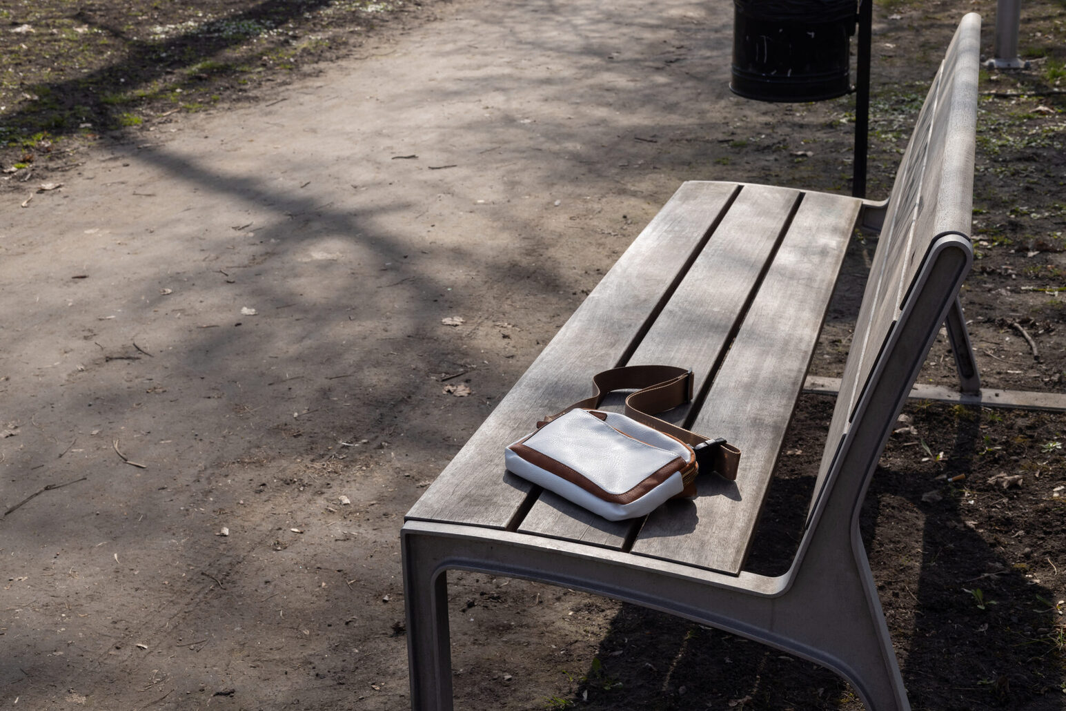 Eine kleine weiß-braune Tasche liegt verlassen auf einer Parkbank