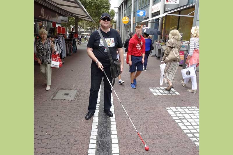 Чоловік з палицею йде по тактильній доріжці в центрі міста.