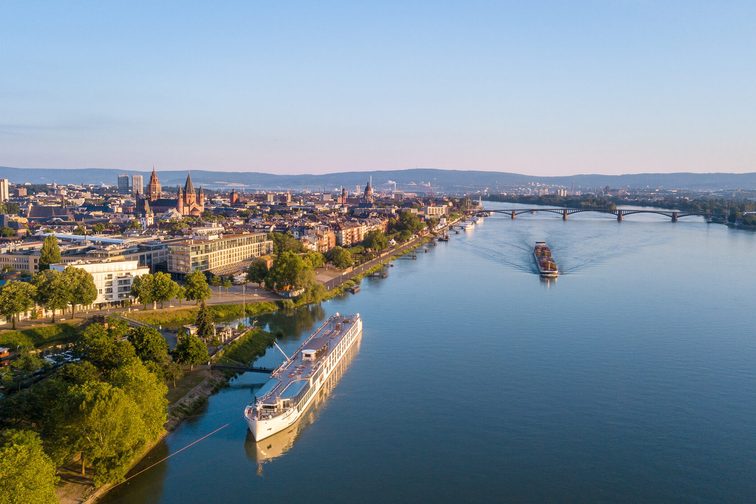 Eine Luftaufnahme der Stadt Mainz kurz vor Sonnenuntergang. In der linken Hälfte des Bildes sieht man die Gebäude der Stadt Mainz und auf der rechten Seite den Rhein.
